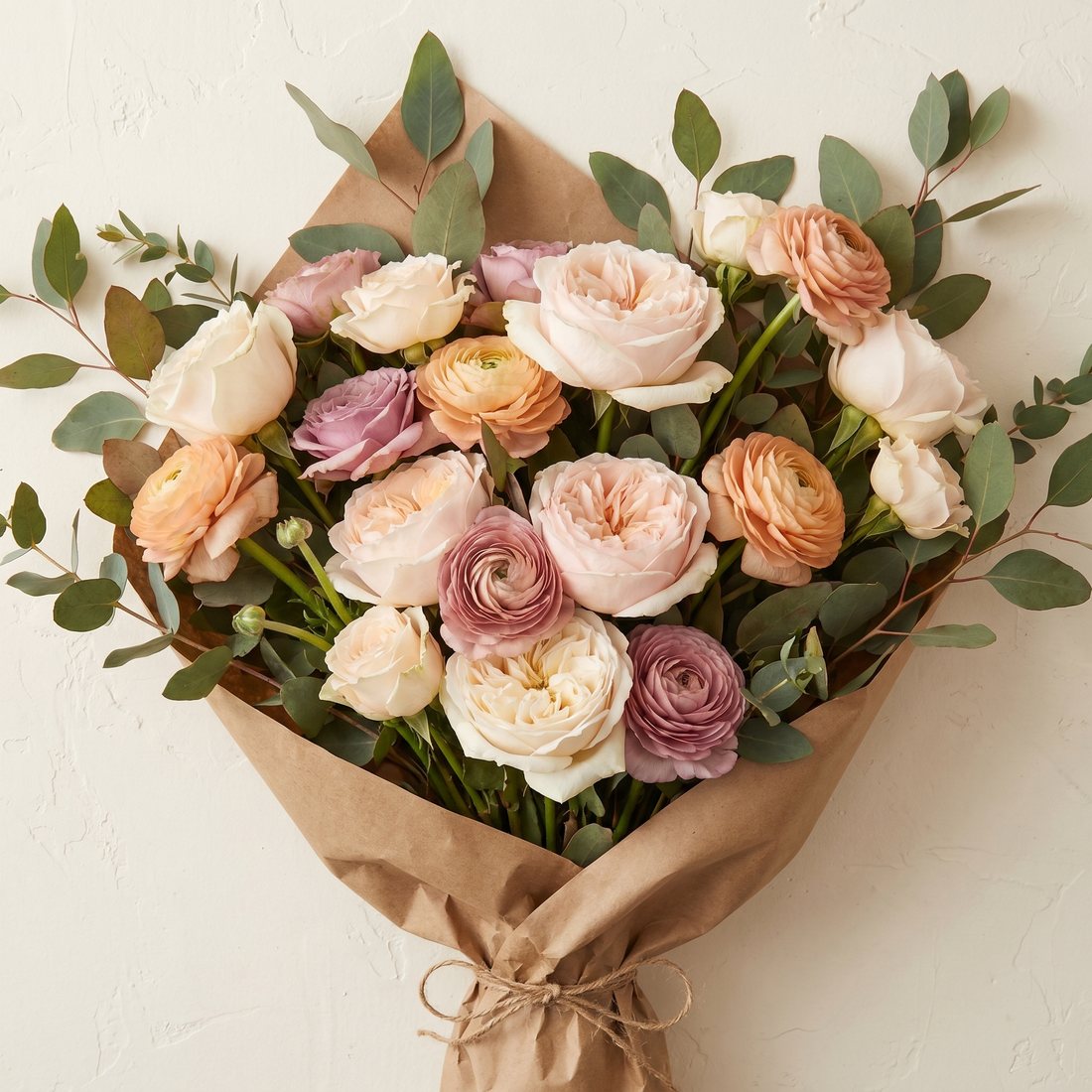 Romantisch los bloemwerk met tuinrozen en ranonkels, verpakt in kraftpapier
